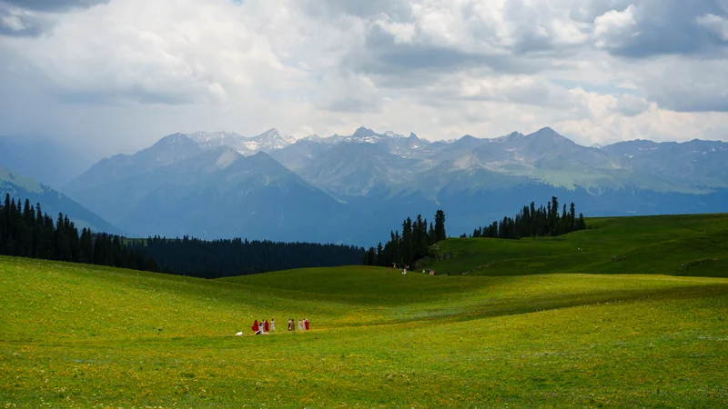 Sunlit green meadows beneath a mountain range and layered clouds.