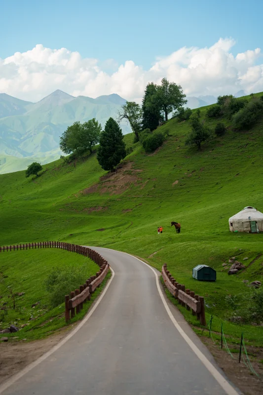 A road curving through green hills toward distant mountains.