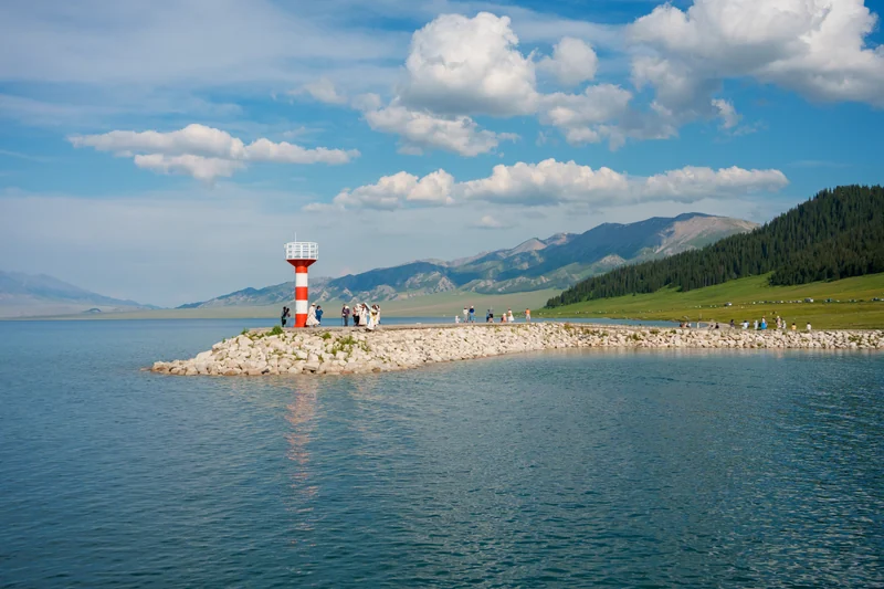 A red and white beacon on a rocky shoreline beside blue water.