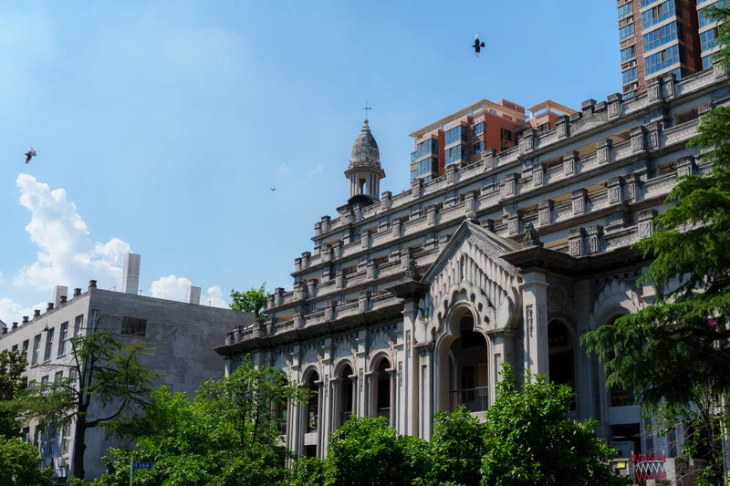 An ornate stone building framed by green foliage and blue sky.