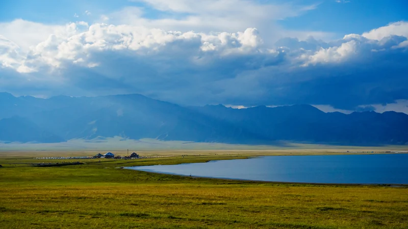 Clouds and changing light above a broad lake and open grassland.