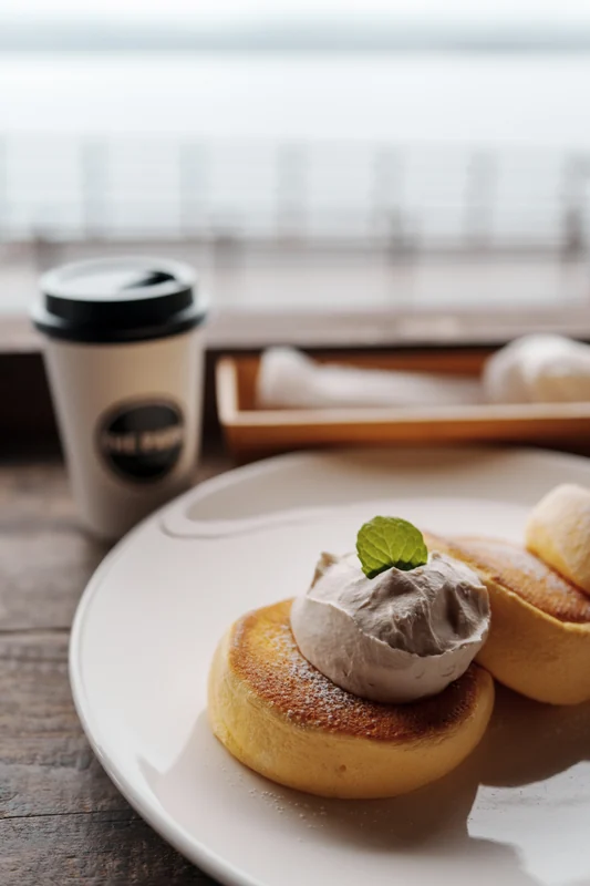Coffee and small pastries on a table beside a window.