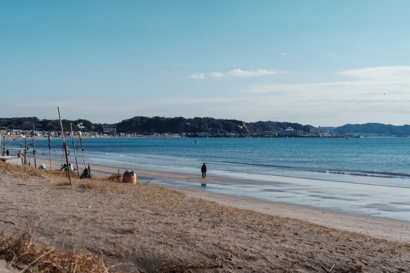 A sandy shoreline and small figures beside a calm blue sea.