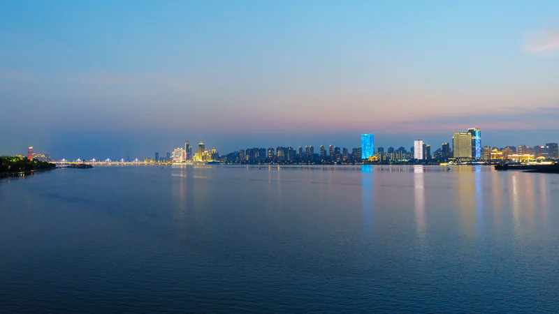 A calm body of water reflecting the evening light of a distant city.
