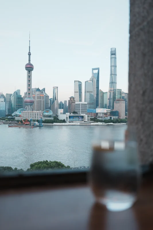 A city skyline across water, seen past an out-of-focus drinking glass.