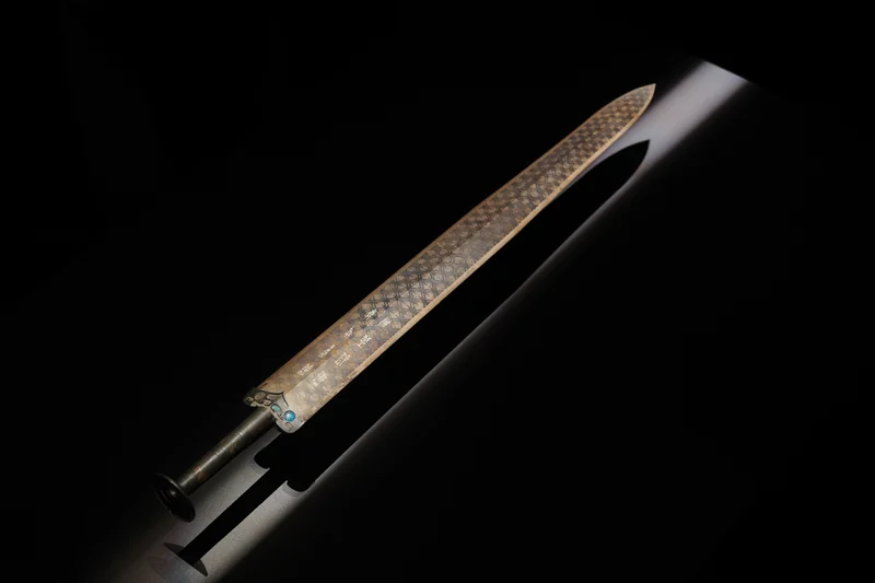 An engraved blade illuminated against a dark background.